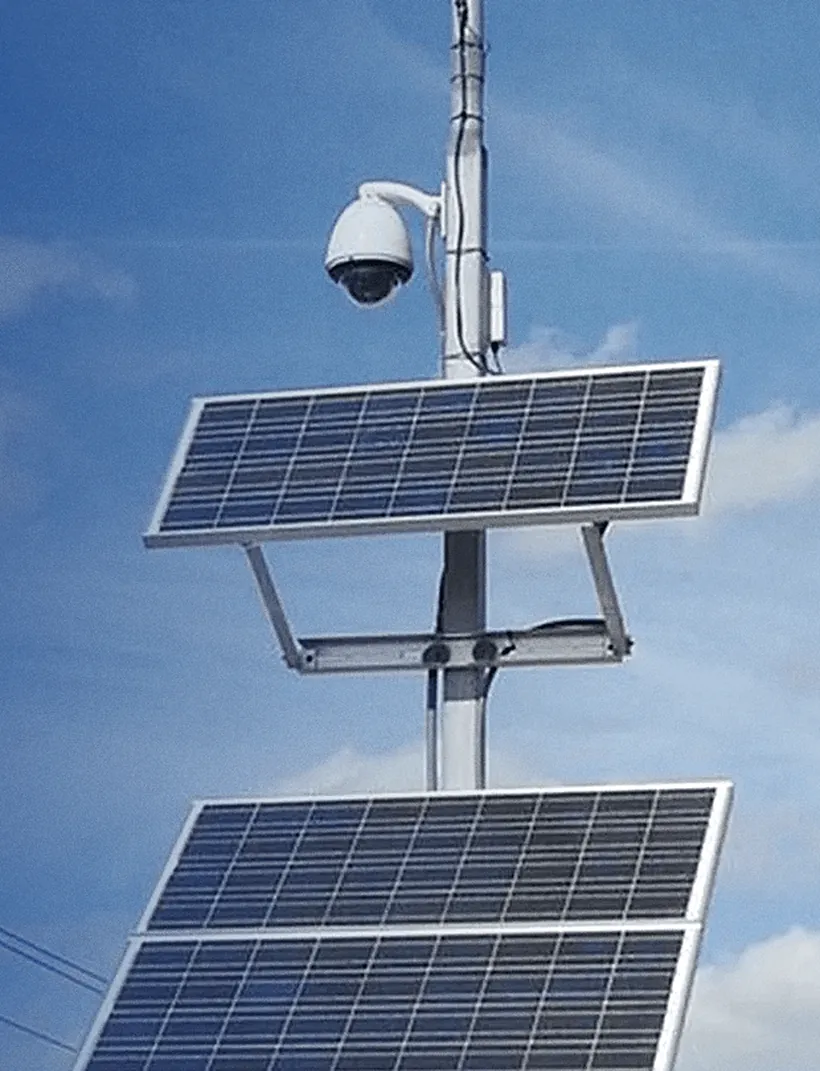 Solar-powered surveillance pole: a PTZ camera above two solar panels against the sky