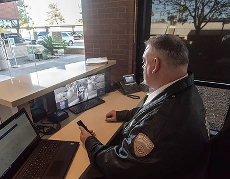 Uniformed guard at a front desk watching a bank of camera monitors