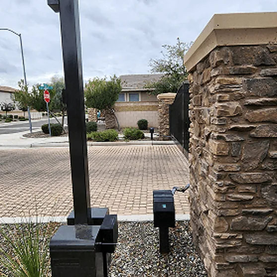 Access pedestal and call-box post beside a stacked-stone pillar at a community entrance