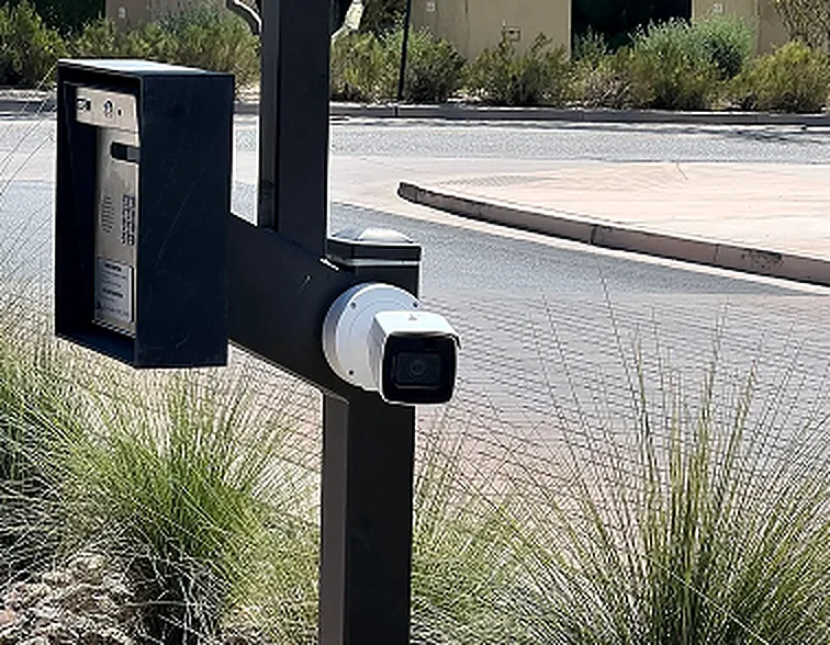 Bullet camera mounted on a steel post beneath a call-box housing at a road entrance