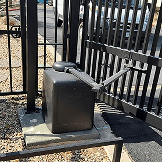 Swing gate operator arm bolted to a concrete pad beside a steel gate